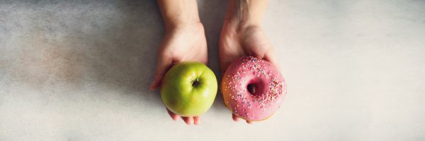 one hand holds a doughnut, the other hand holds an apple